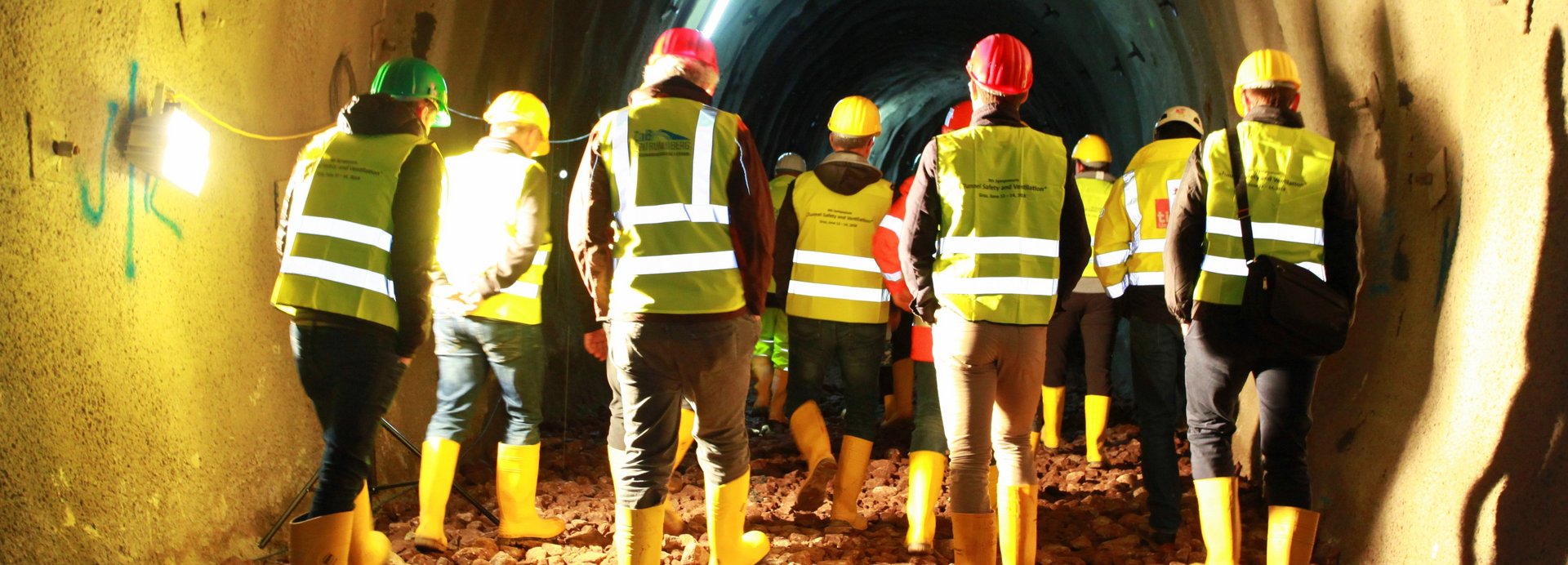 In einem beleuchteten Tunnel bewegen sich Menschen mit Warnweste fort.