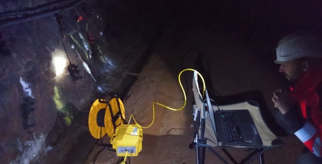 Abgebildet ist ein dunkler Tunnel, worin sich ein Mann befindet mit verschiedenen Utensilien und einem Laptop am Boden hockt.