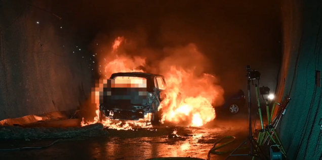 Ein brennendes (zensiertes) Auto steht in einem dunklen Tunnel.